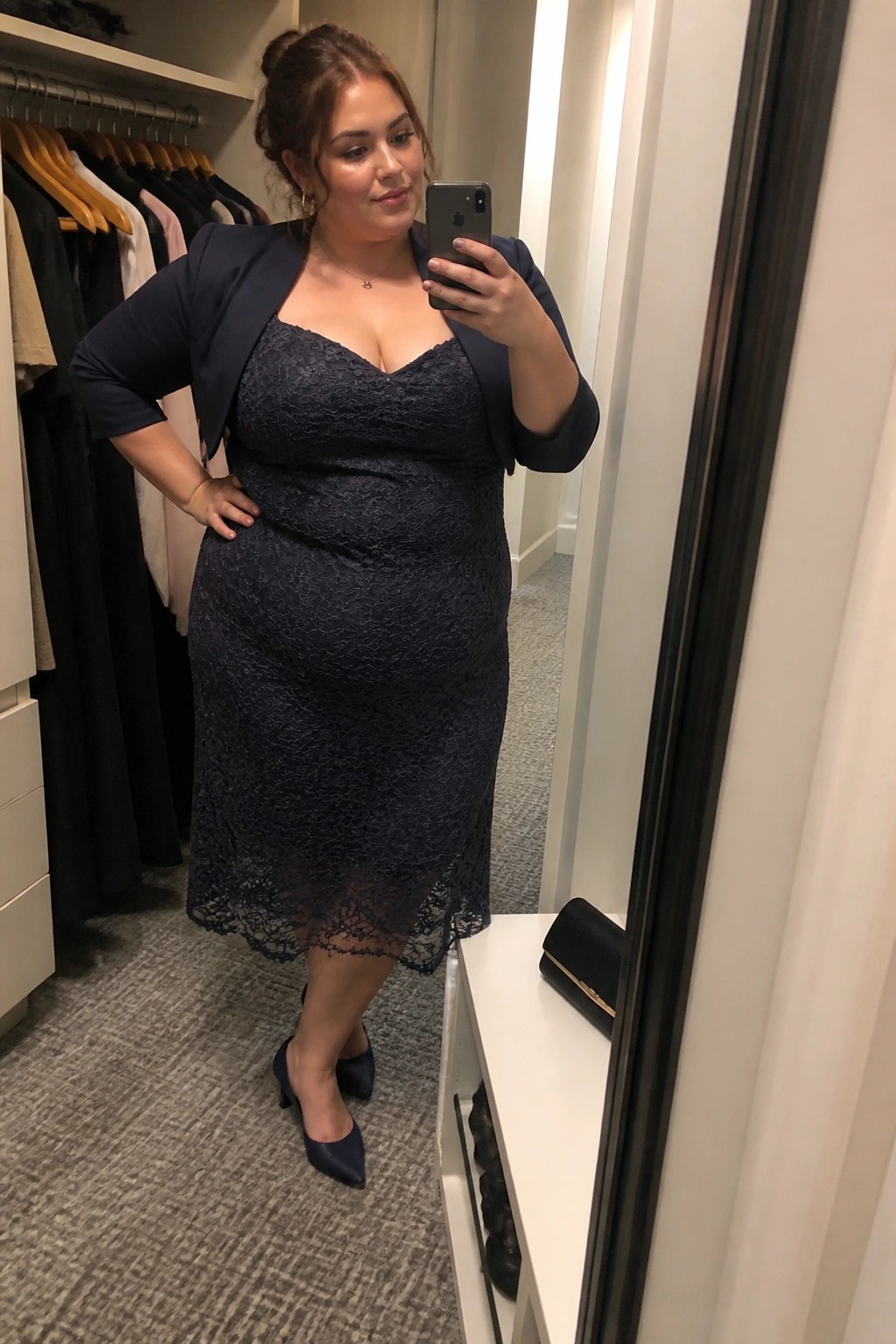 Plus size woman wearing a navy lace midi dress under a matching navy blazer with navy pointed toe heels and delicate gold jewelry in a mirror selfie.
