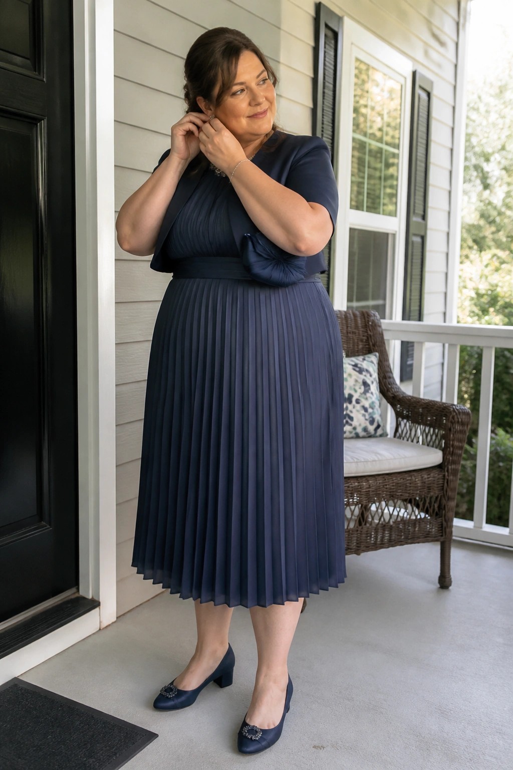 Woman in navy pleated midi dress with bow adjusts earring on porch