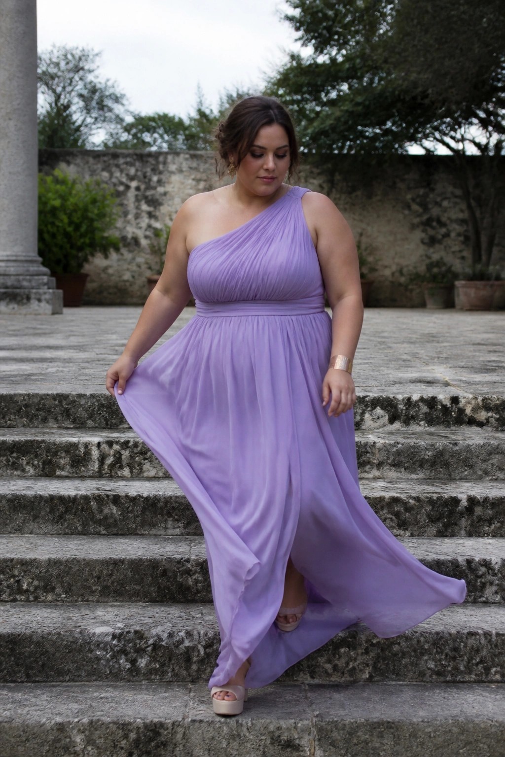 Woman in flowing lavender one-shoulder gown on stone outdoor steps