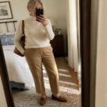 Woman in cream turtleneck sweater tucked into taupe straight-leg trousers, paired with brown suede loafers and a matching leather tote bag, shown in a full-length mirror selfie