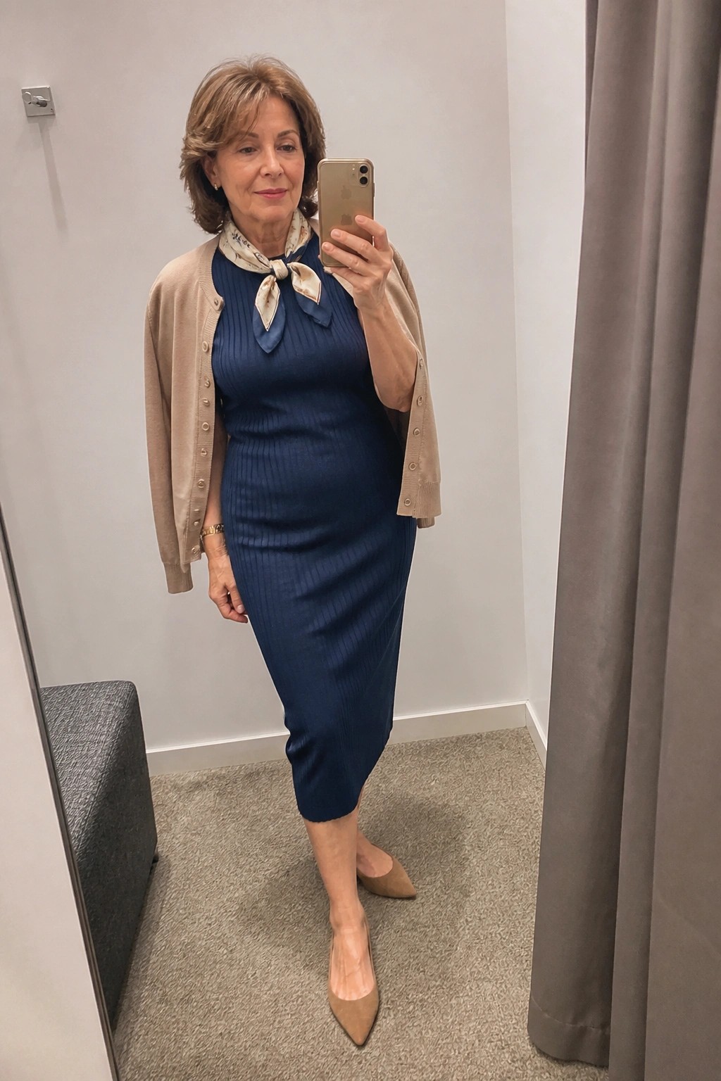 Woman in navy blue dress and beige cardigan taking mirror selfie