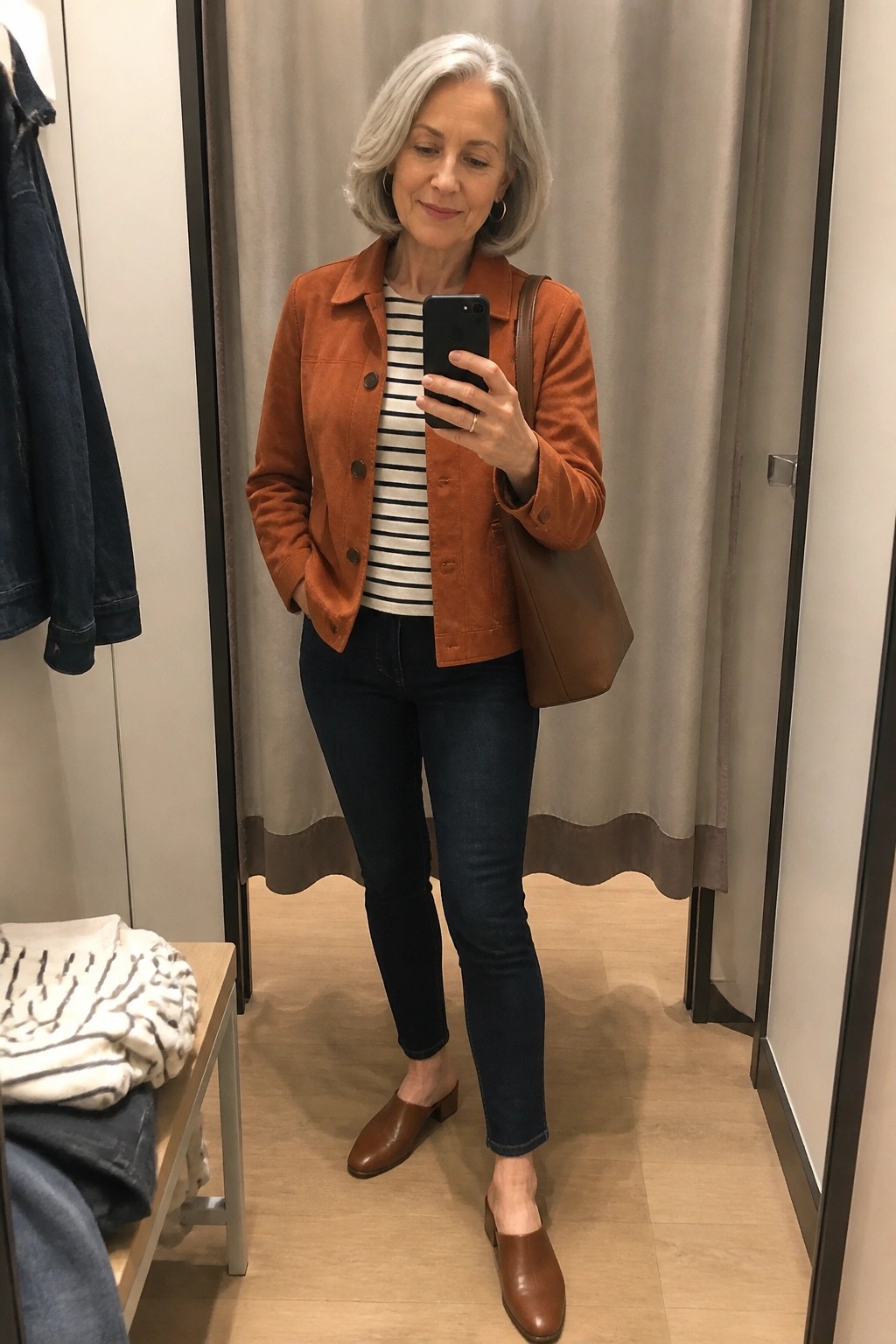 Woman with gray hair in orange jacket taking mirror selfie in fitting room