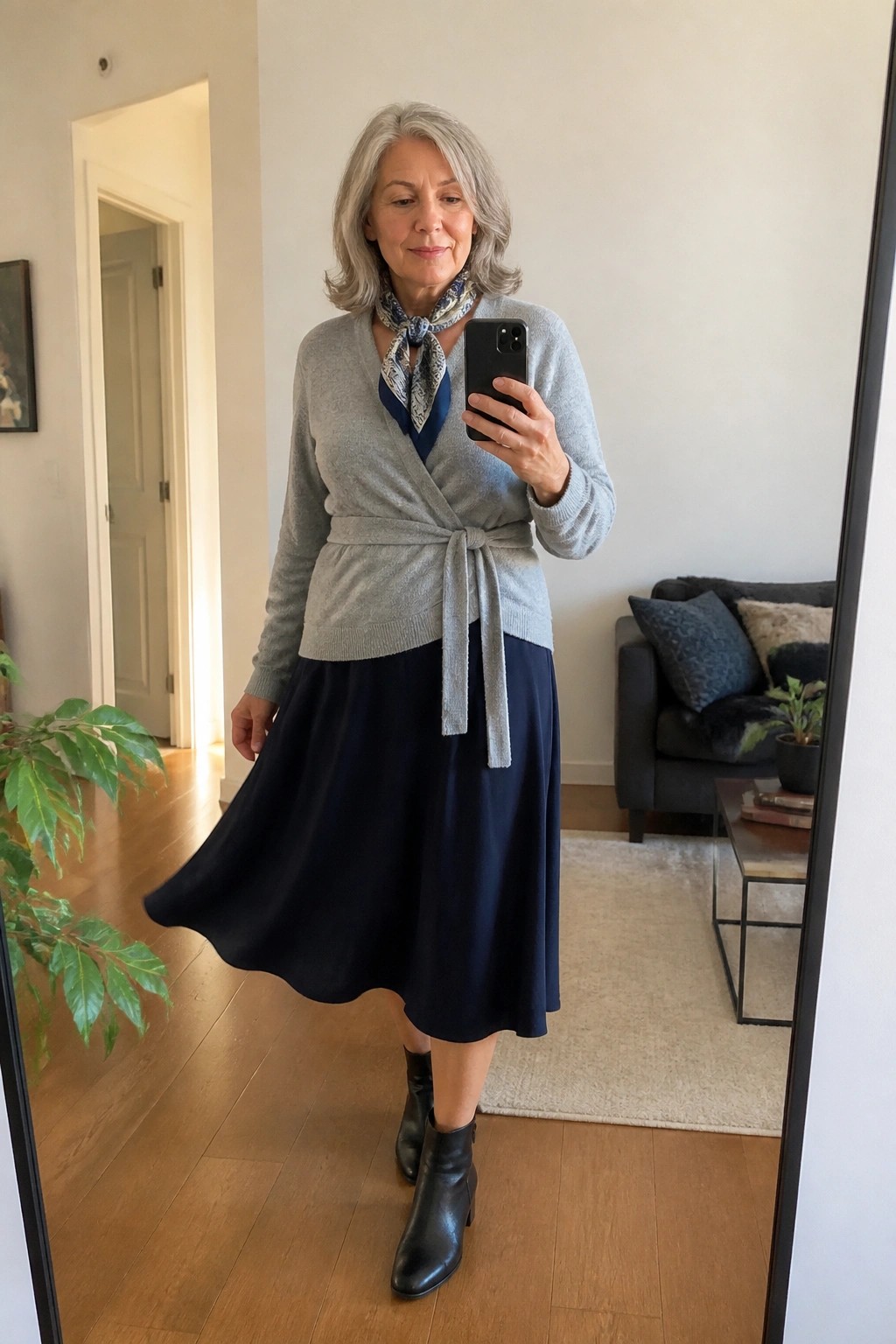 Silver-haired woman in gray wrap sweater and navy skirt taking mirror selfie