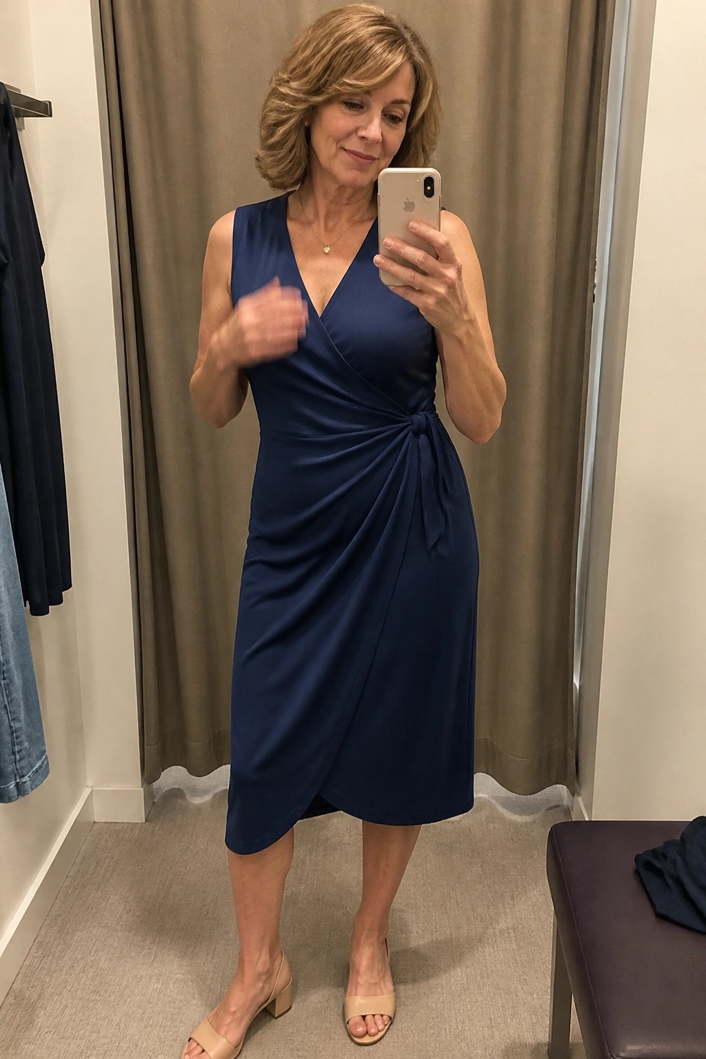 Woman in navy blue wrap dress taking mirror selfie in fitting room