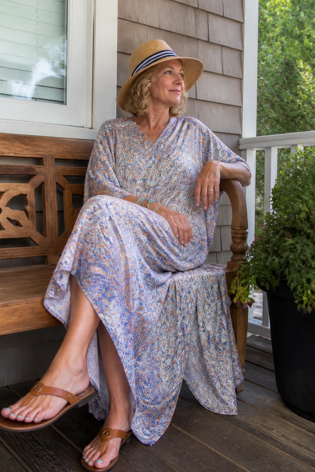 Woman in floral dress and straw hat seated on wooden porch bench