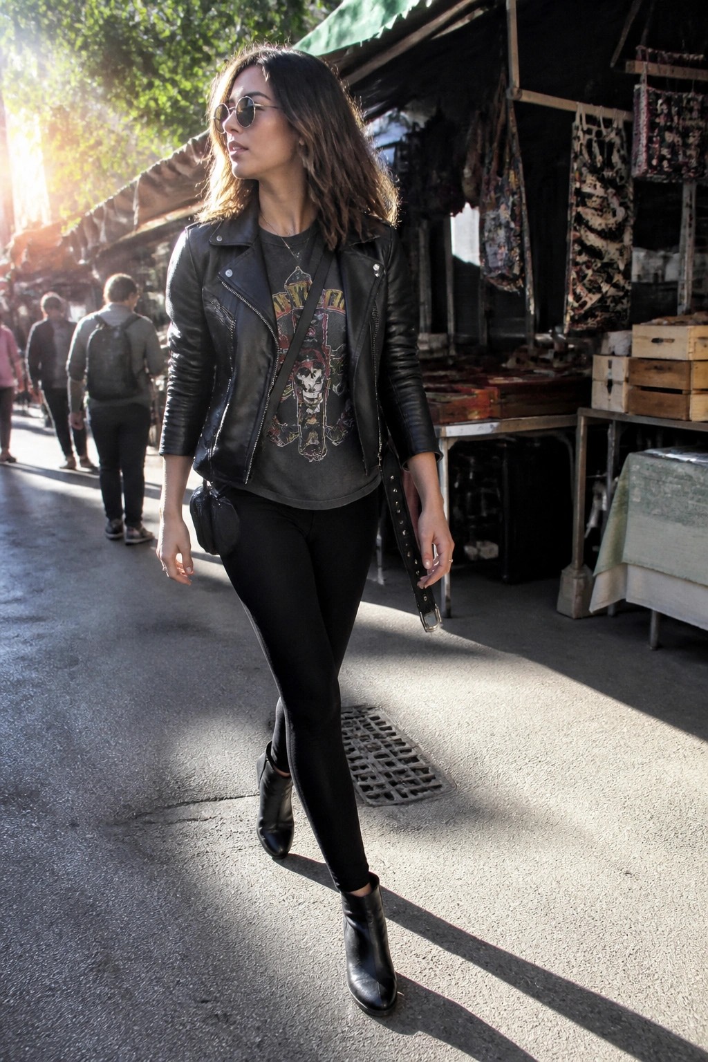 Woman in black leather jacket and sunglasses walking sunny outdoor market street
