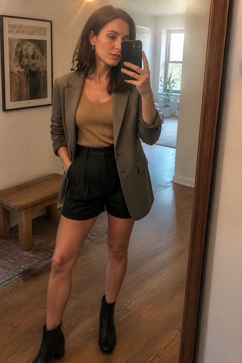 Woman in gray blazer and black shorts taking mirror selfie with phone