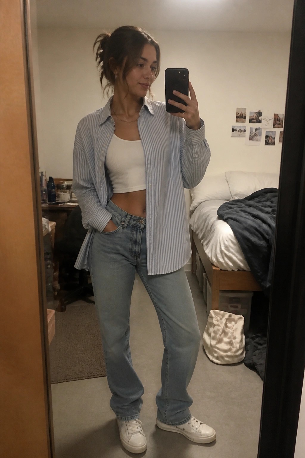 Woman in striped shirt and jeans taking bedroom mirror selfie