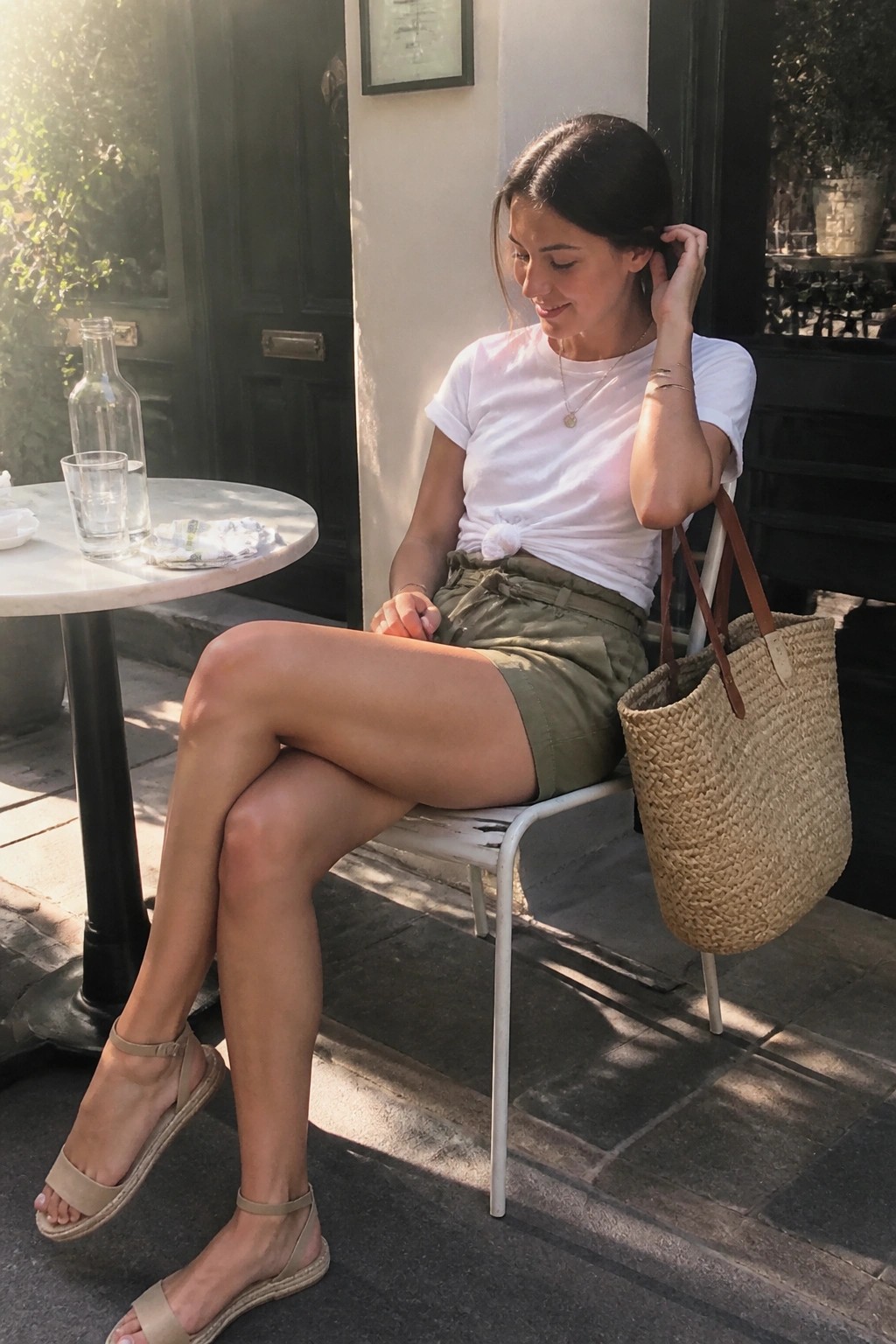 Woman in white tied t-shirt and olive shorts with woven straw bag in sunlight