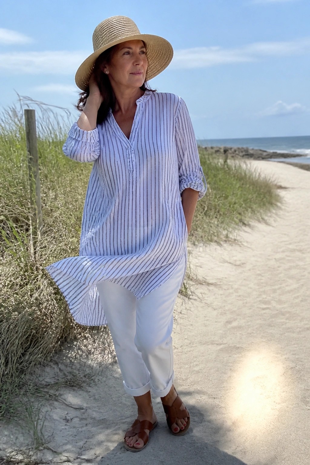 Woman in striped blouse and white pants wearing straw hat on sunny beach path