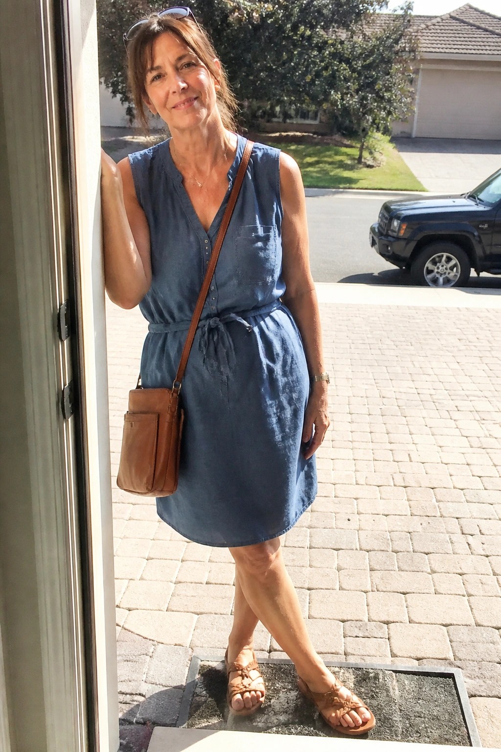 Woman in blue denim dress with brown bag standing in doorway.