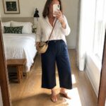 Woman in white shirt and navy wide-leg pants with woven bag taking mirror selfie