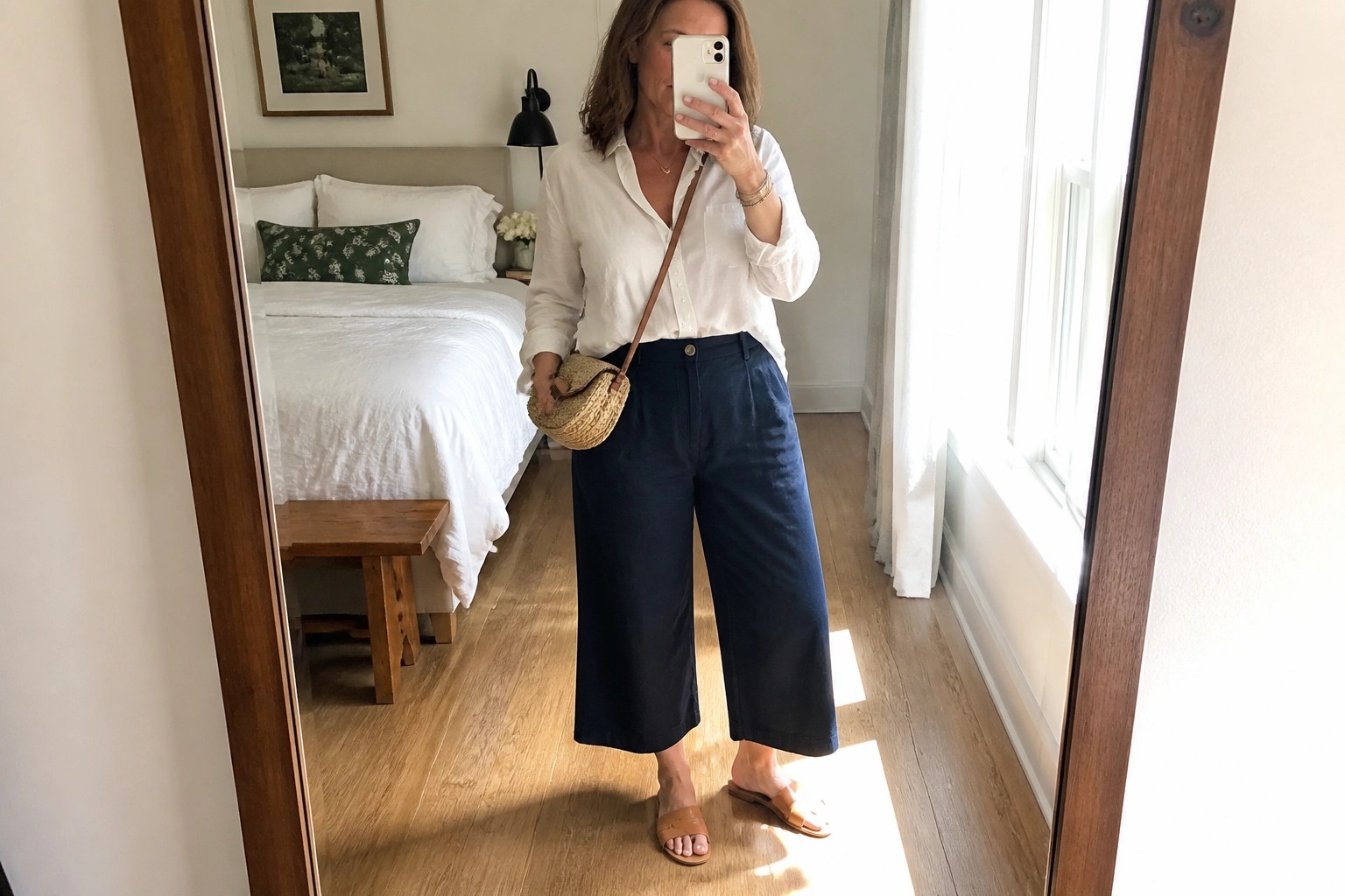 Woman in white shirt and navy wide-leg pants with woven bag taking mirror selfie