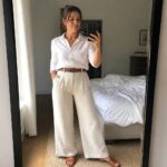 Woman in white shirt and beige wide-leg pants taking mirror selfie in bedroom