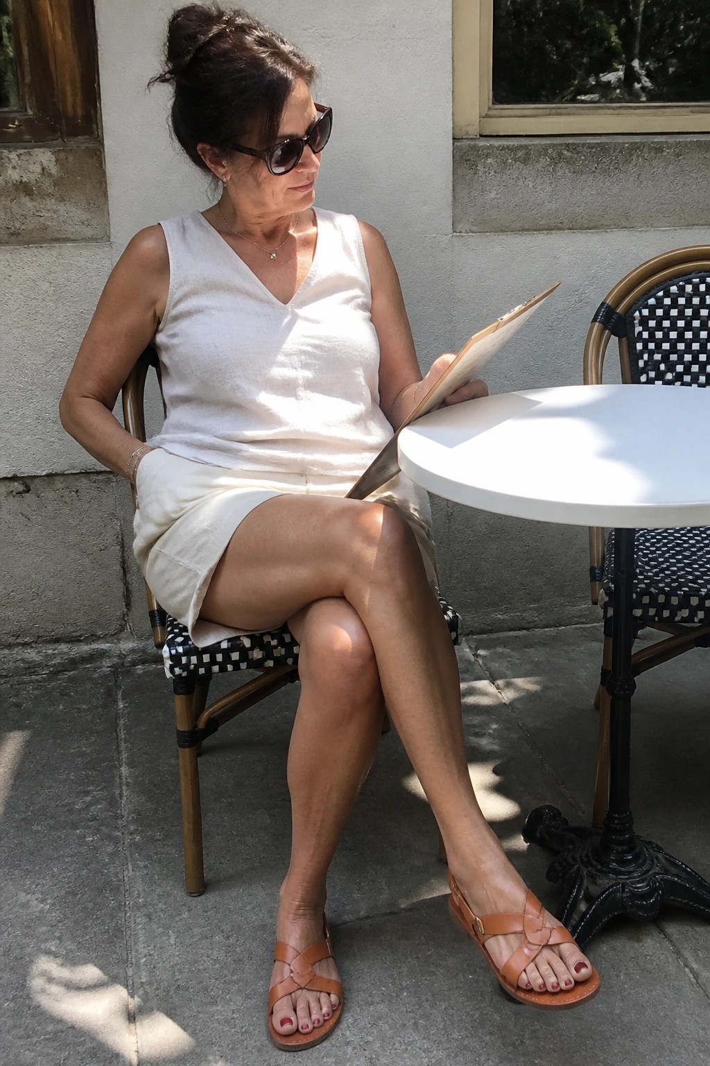 Woman in white linen top and skirt reads menu at sunny outdoor cafe table