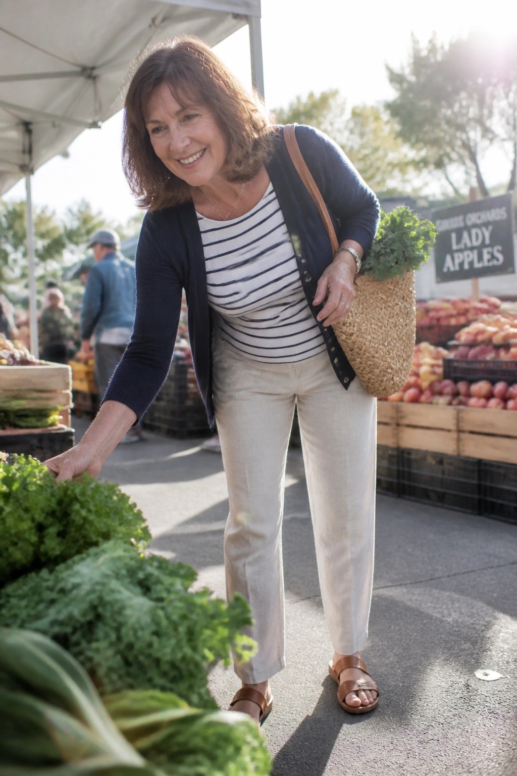 Smiling woman in striped shirt reaches for kale at sunny market stall