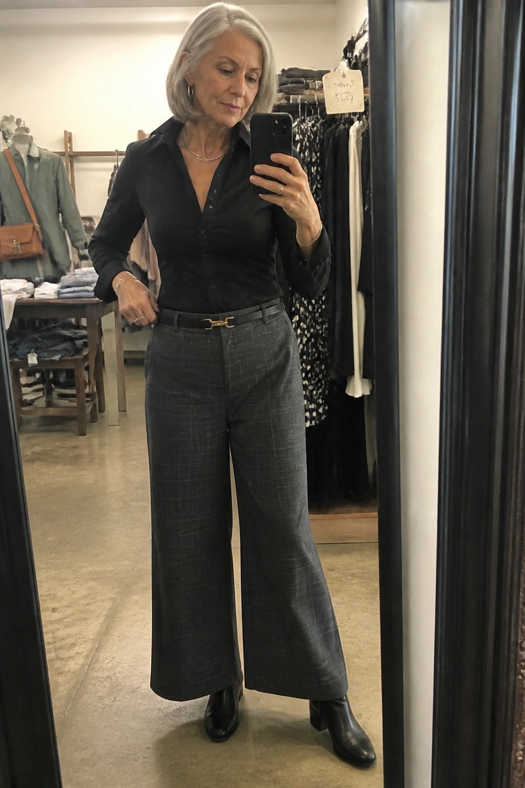 Gray-haired woman in black shirt and gray plaid wide-leg pants taking mirror selfie