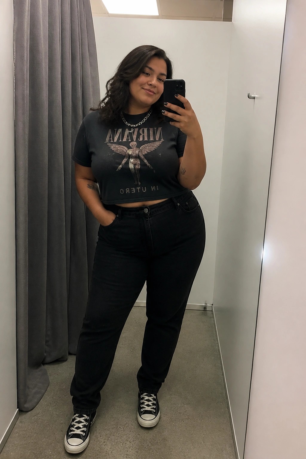 Woman in black Nirvana crop top and jeans taking mirror selfie with phone