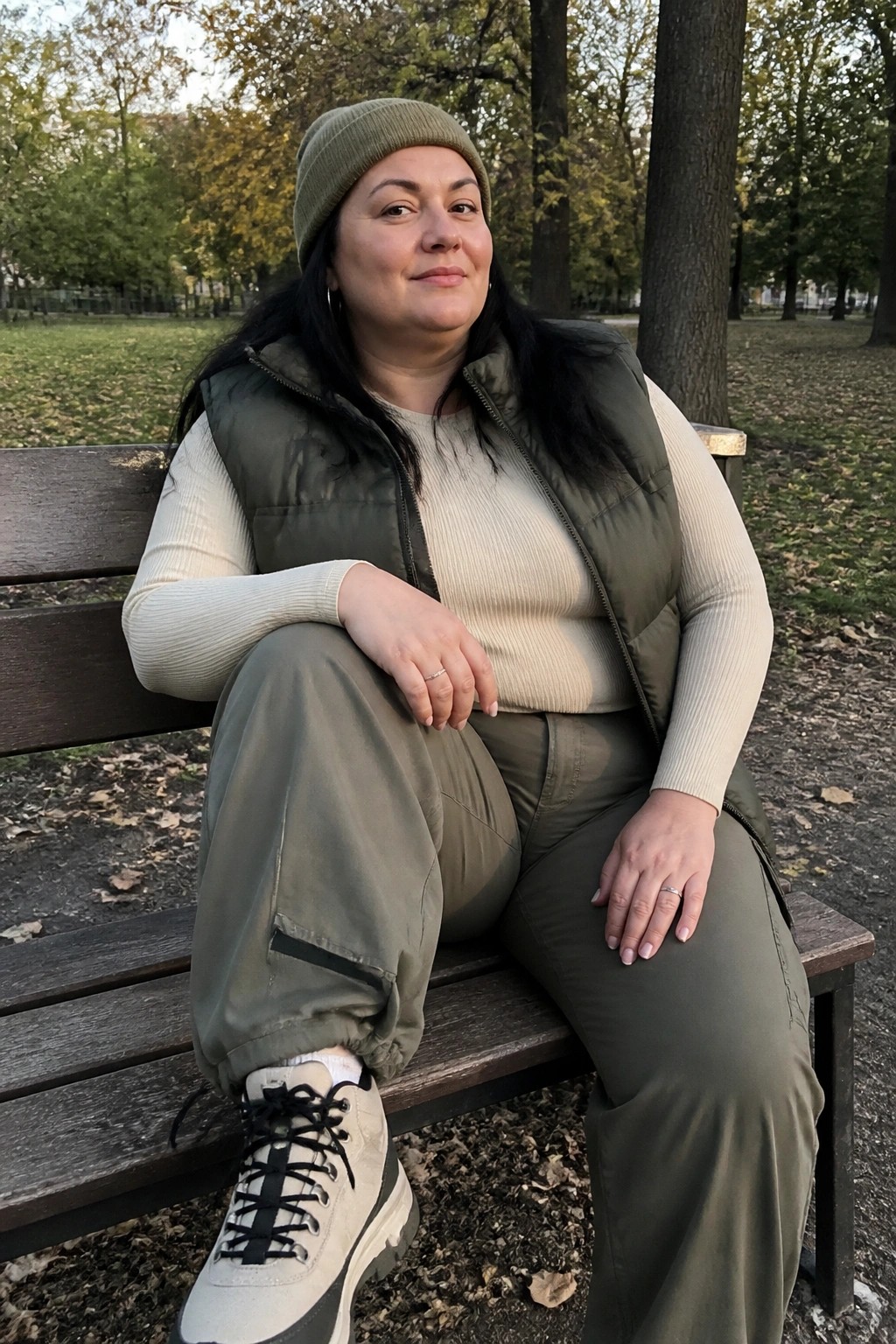 Woman in green beanie and puffer vest seated on wooden park bench