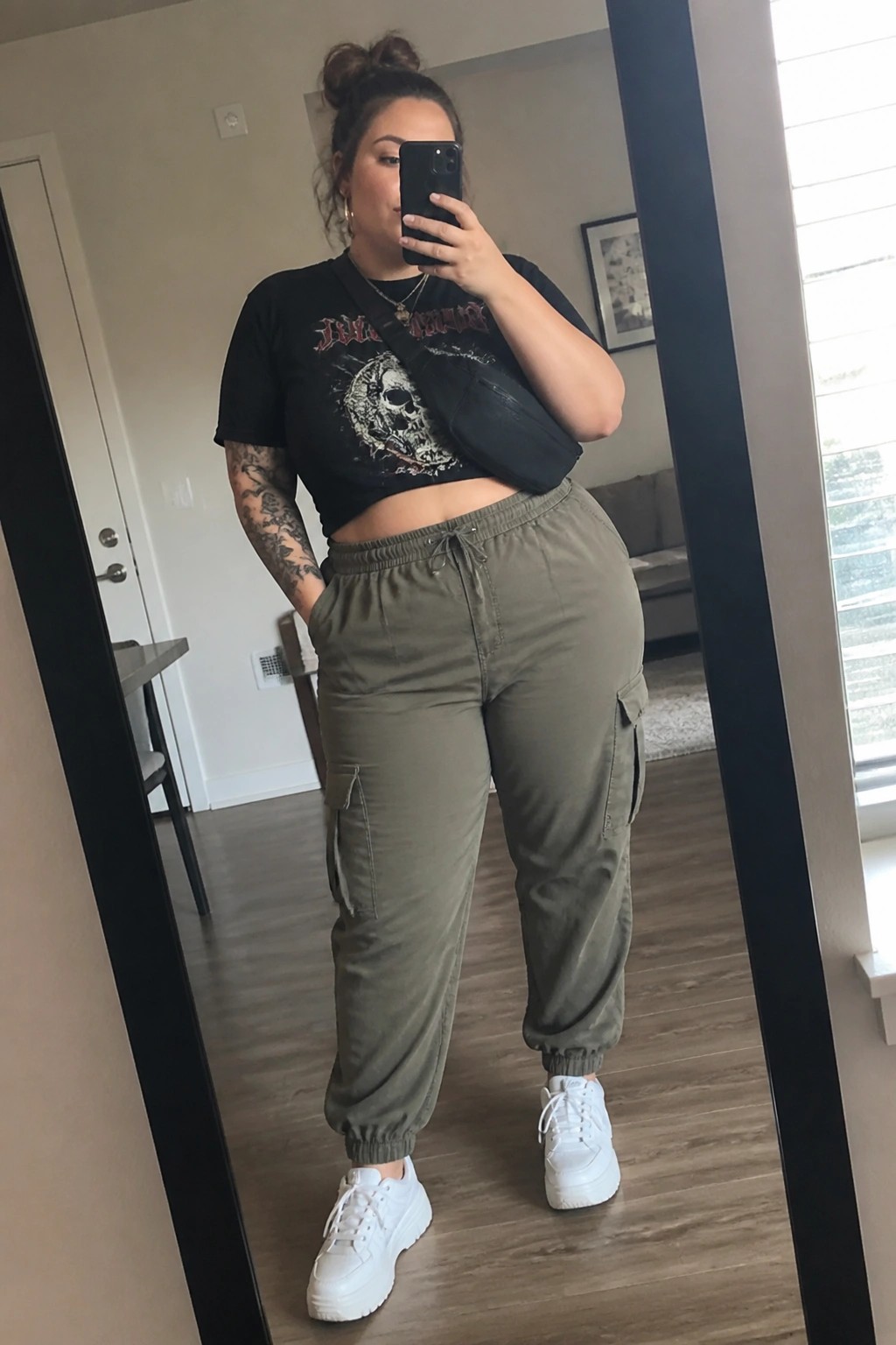 plus size woman in black cropped graphic tee olive cargo joggers and white sneakers taking mirror selfie
