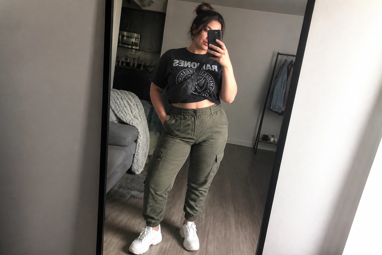 plus size woman in black cropped graphic tee olive cargo joggers and white sneakers taking mirror selfie