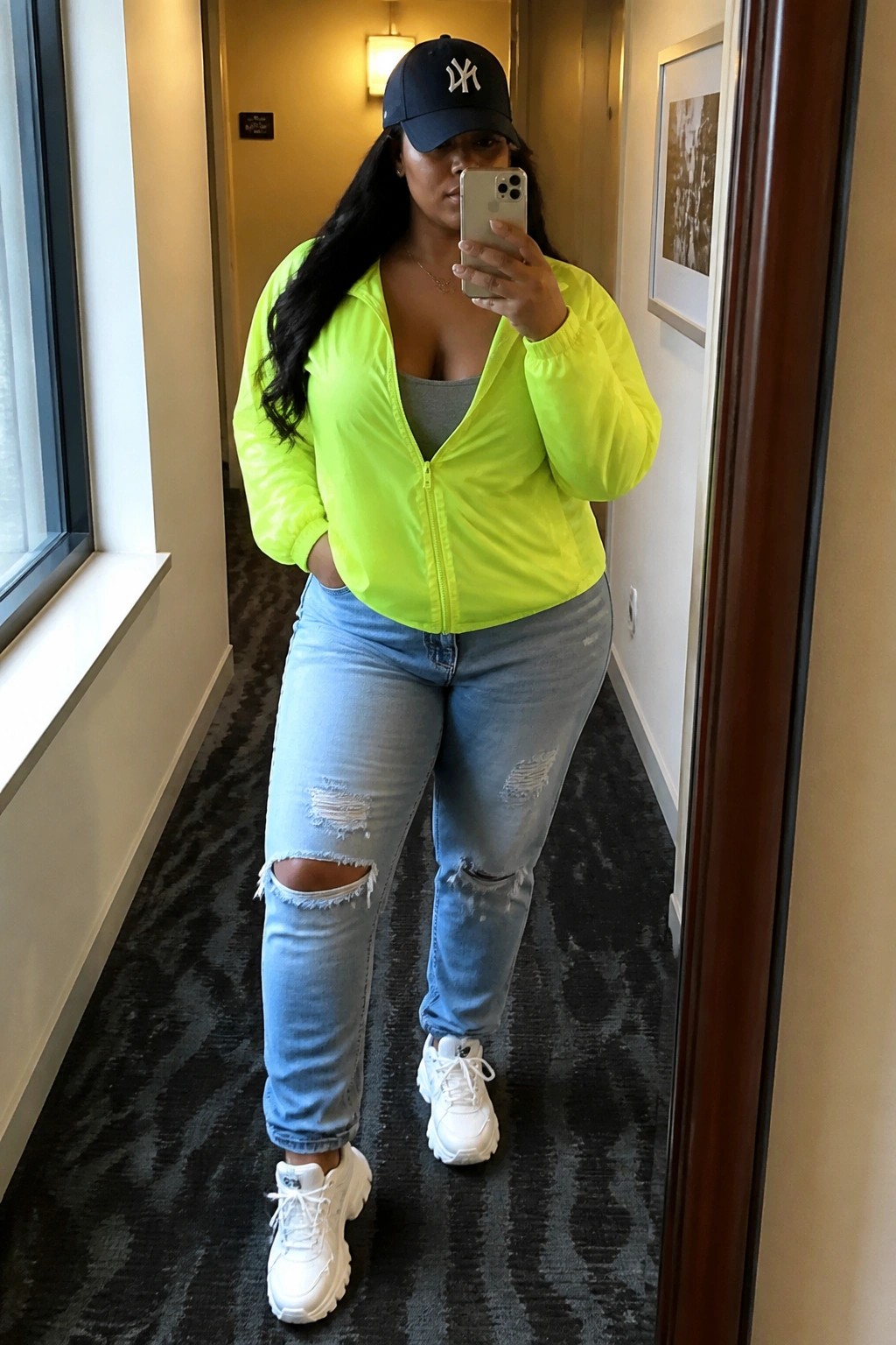 Woman in neon yellow jacket and ripped jeans taking hallway mirror selfie