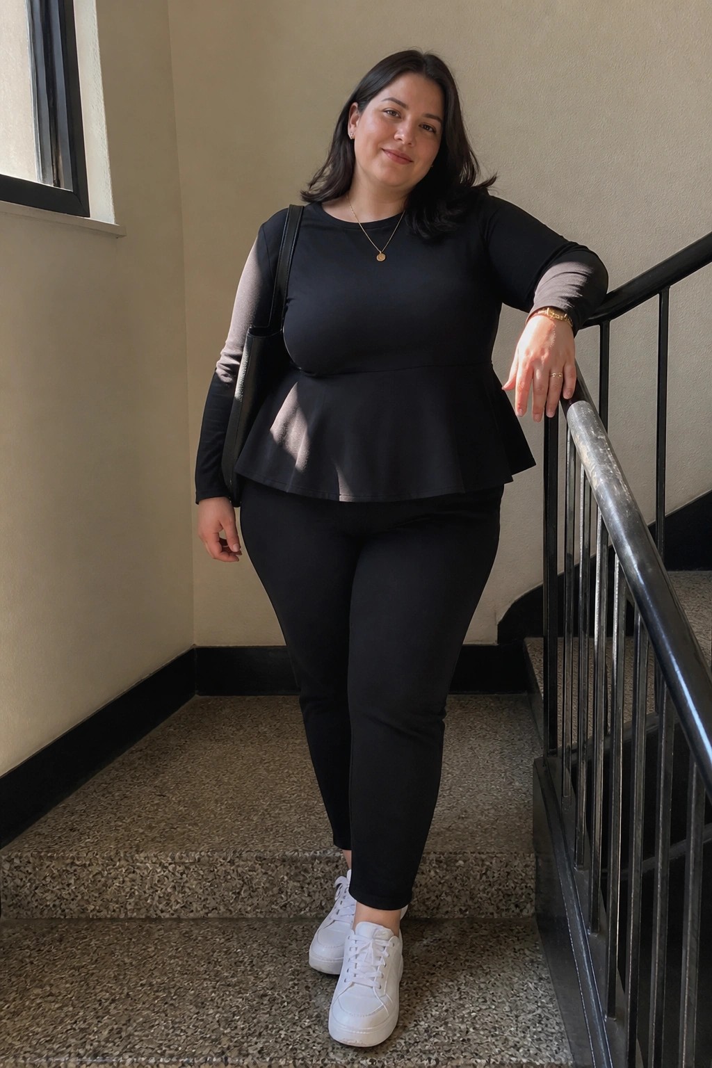 Woman in black peplum top and leggings leaning on stair railing with white sneakers