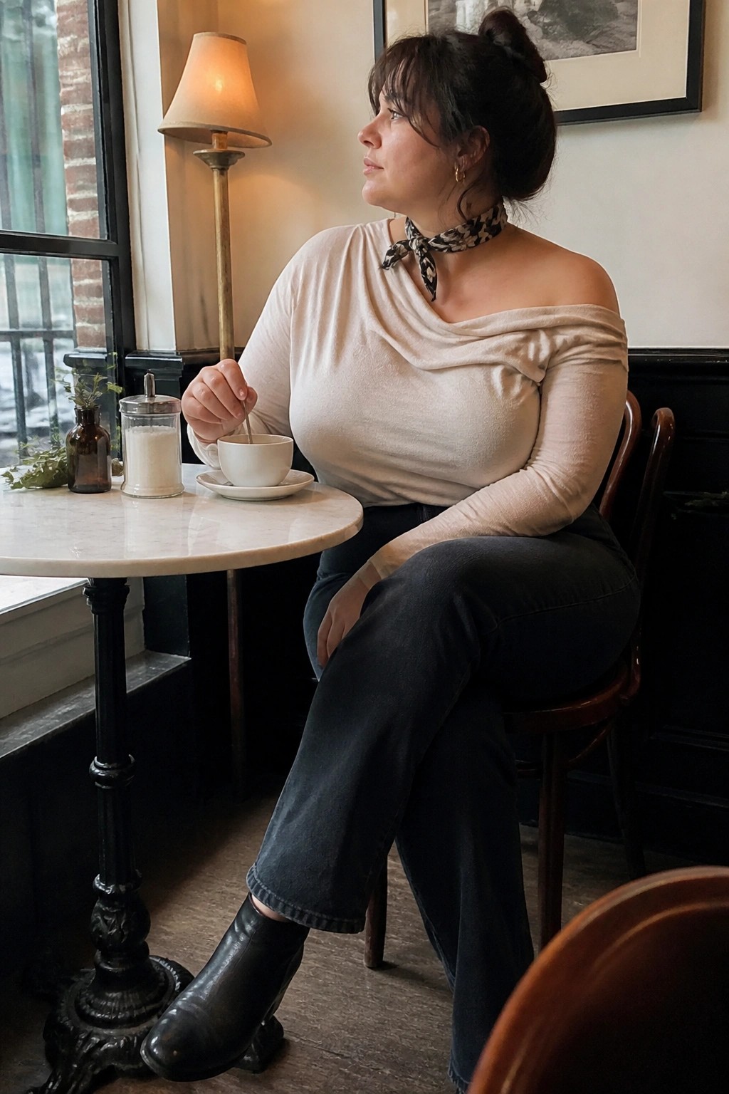 Woman in beige off-shoulder top stirs coffee at marble cafe table