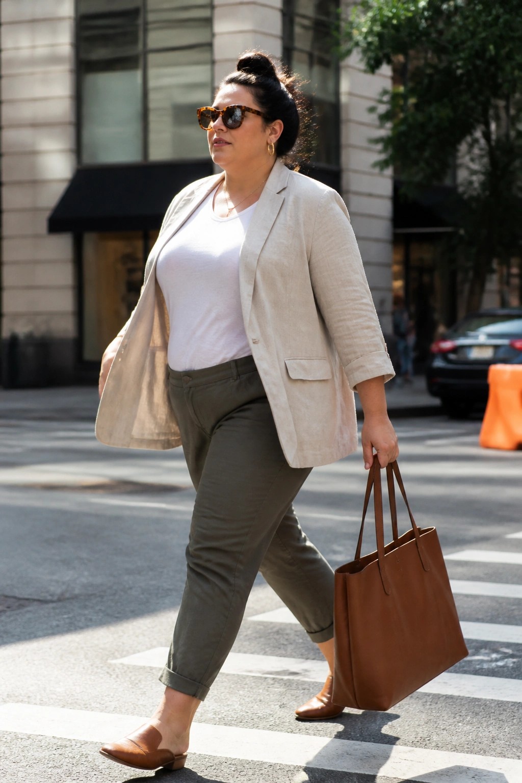 Woman in beige blazer and green pants crossing street with brown tote bag