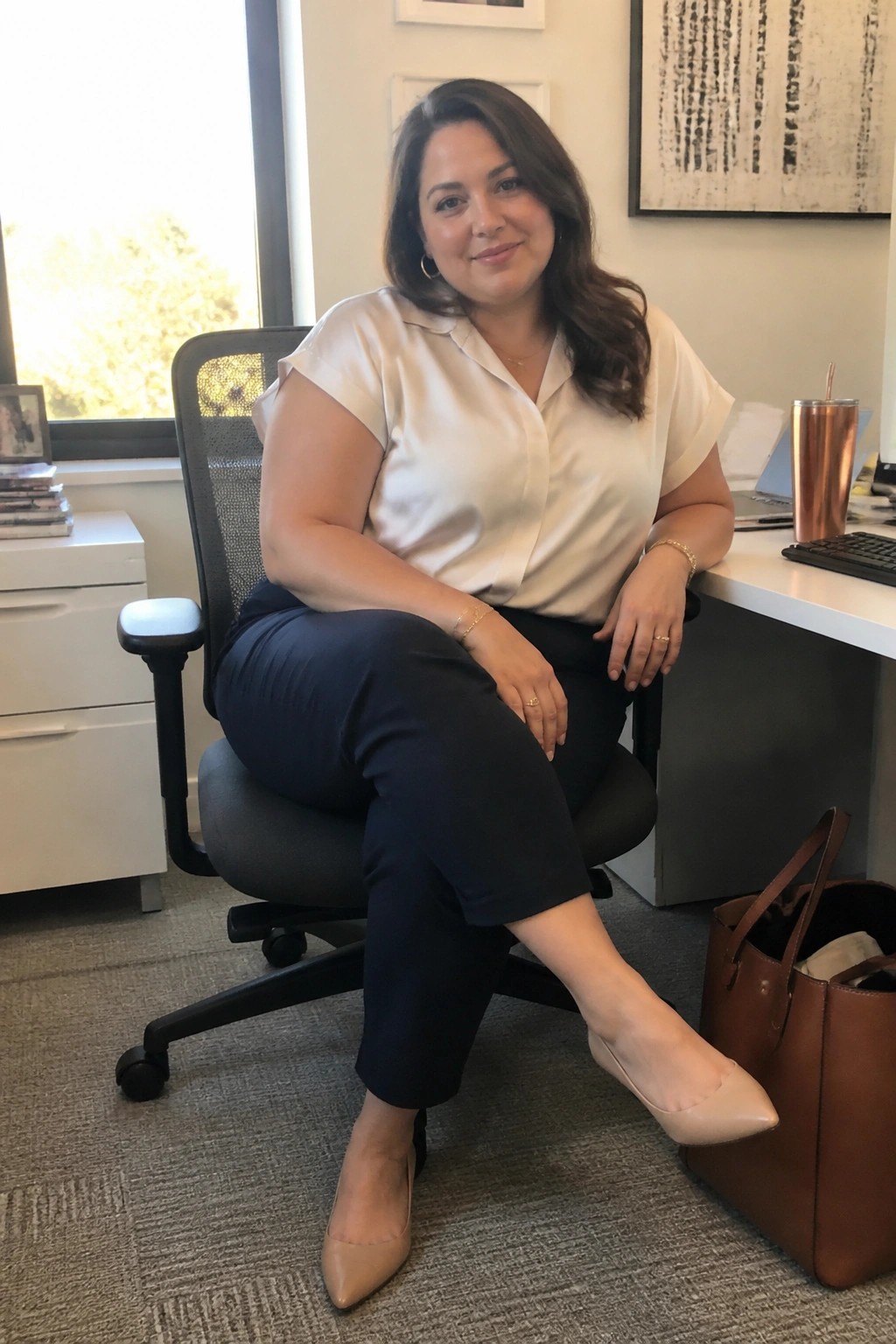 Woman in cream blouse and navy pants seated in black office chair