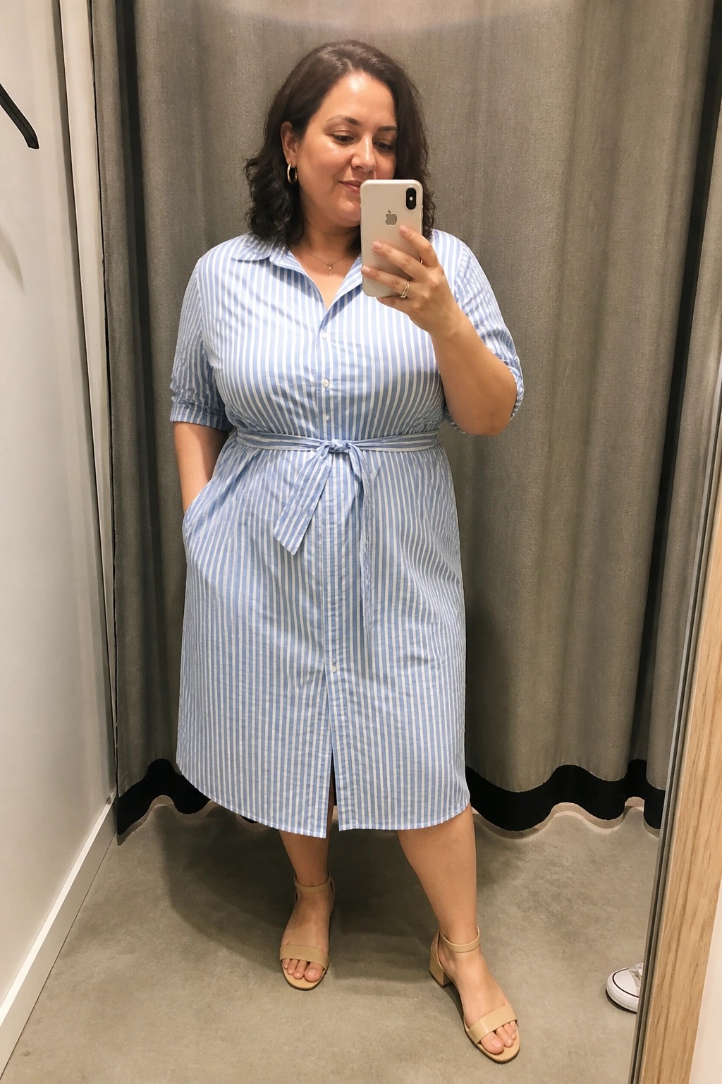 Woman in blue striped shirt dress taking mirror selfie in fitting room