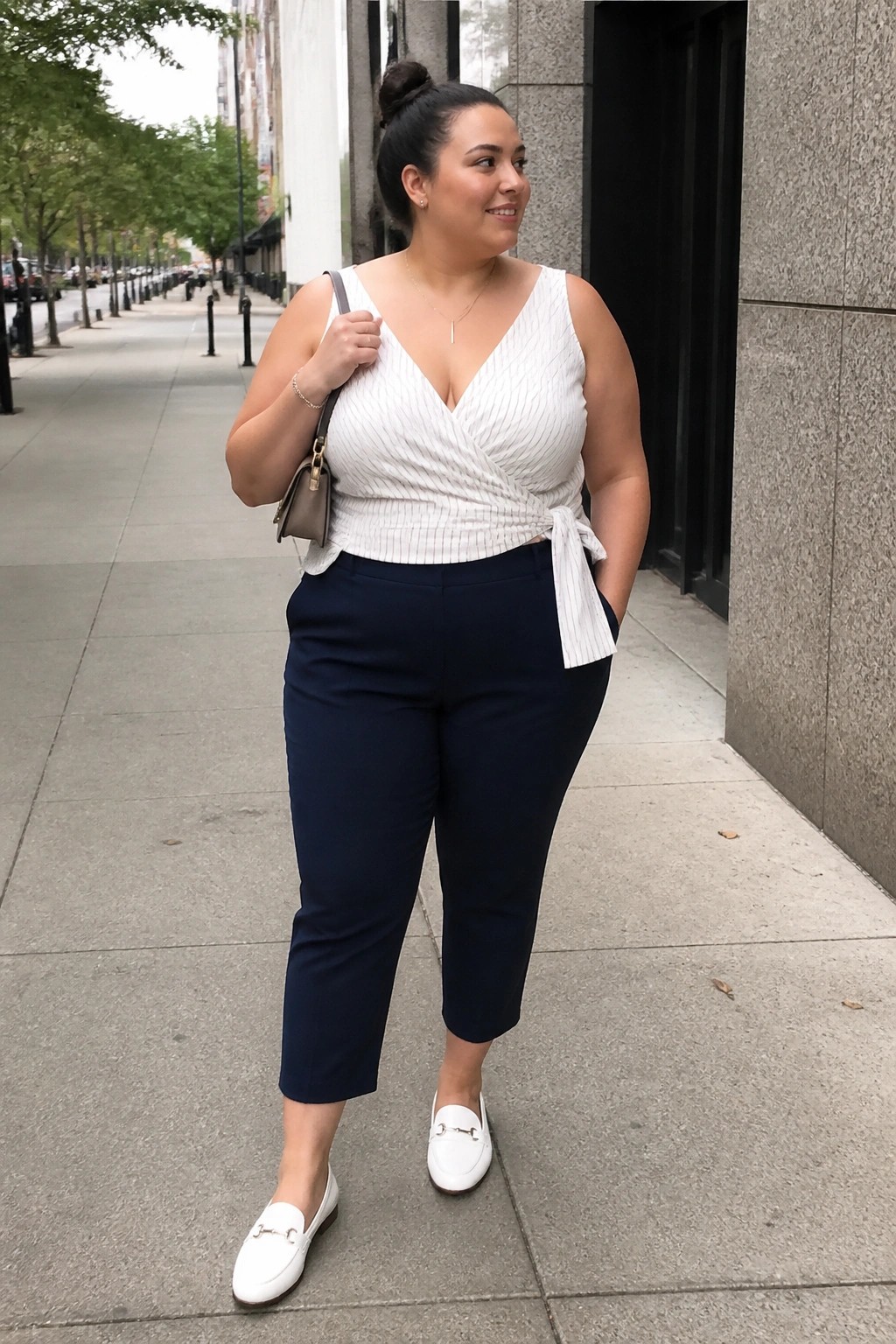 Woman in white striped wrap top and navy capri pants on city sidewalk