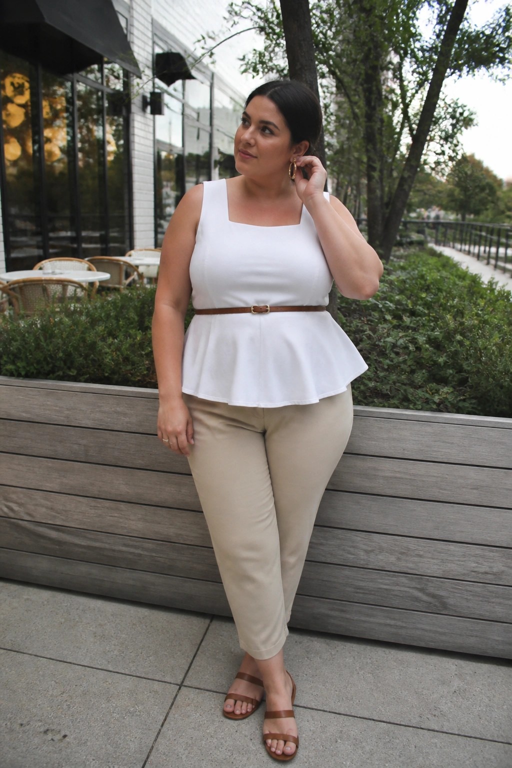 Woman in white peplum top with brown belt and beige pants outdoors.