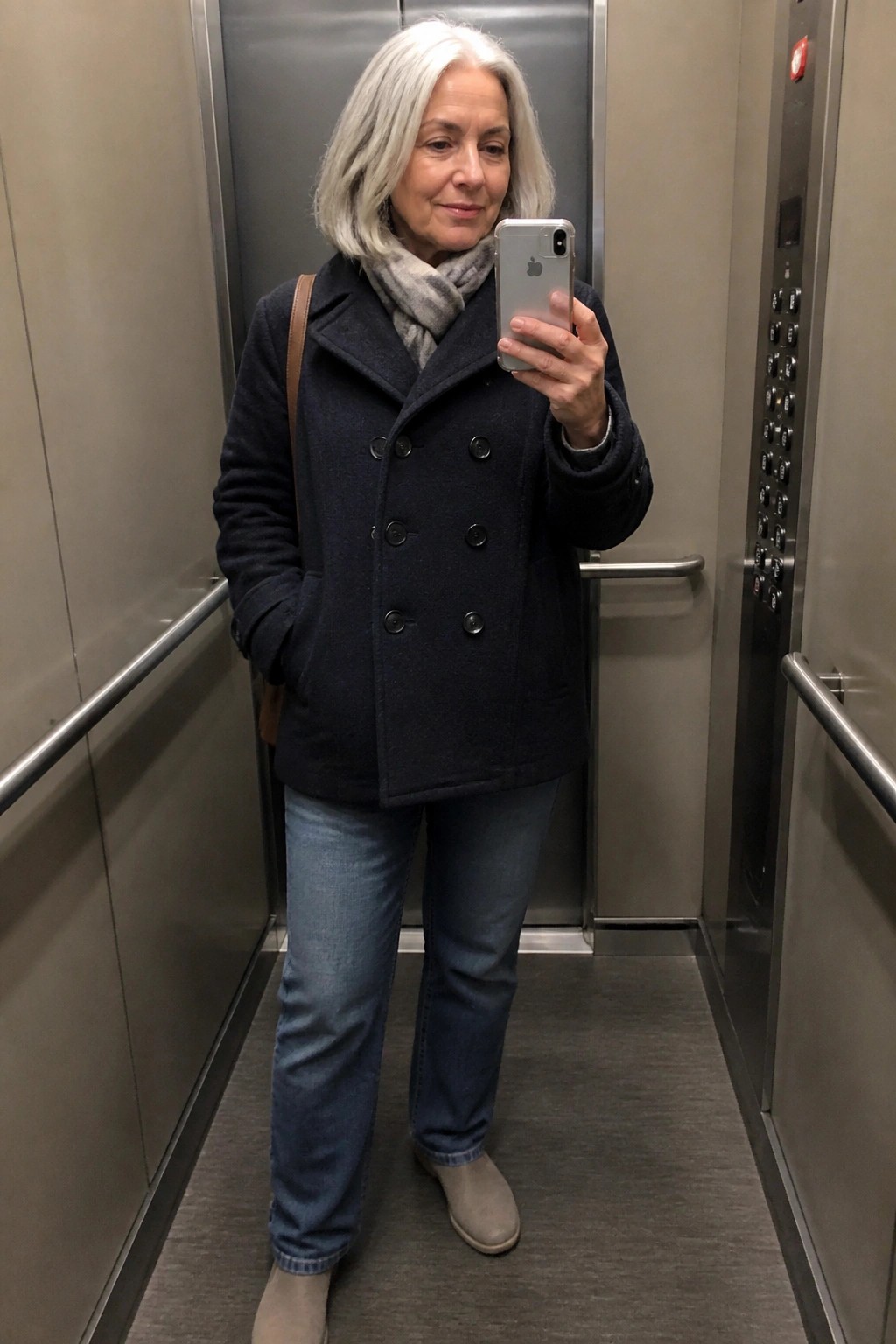 Woman with gray hair in navy coat taking selfie in elevator