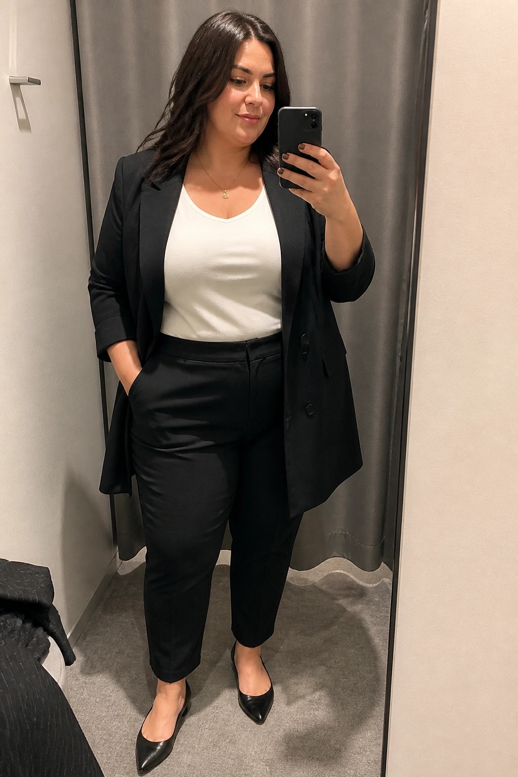 Woman in black blazer over white top taking mirror selfie with phone