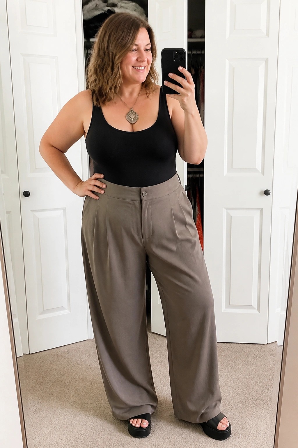 Woman in black tank top and taupe wide-leg pants taking mirror selfie