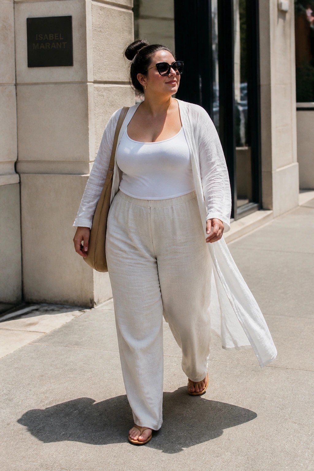 Woman in white tank top, wide pants, and long cardigan walking on sidewalk
