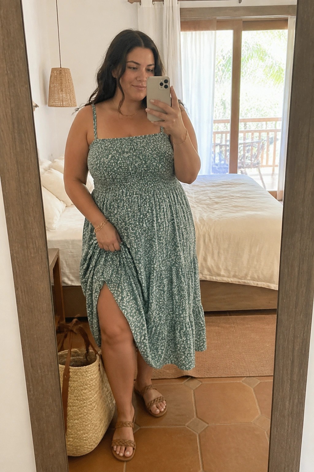 Woman in green floral dress taking mirror selfie in bedroom with woven bag