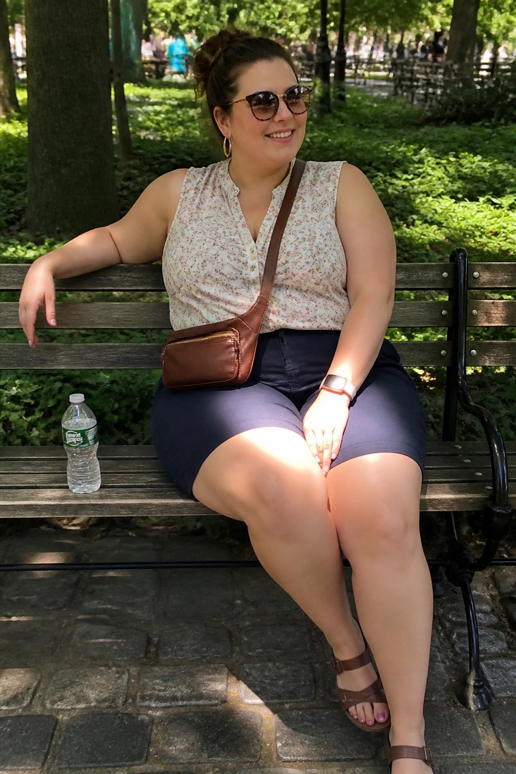 Smiling woman in floral top and blue shorts on sunny park bench with water bottle