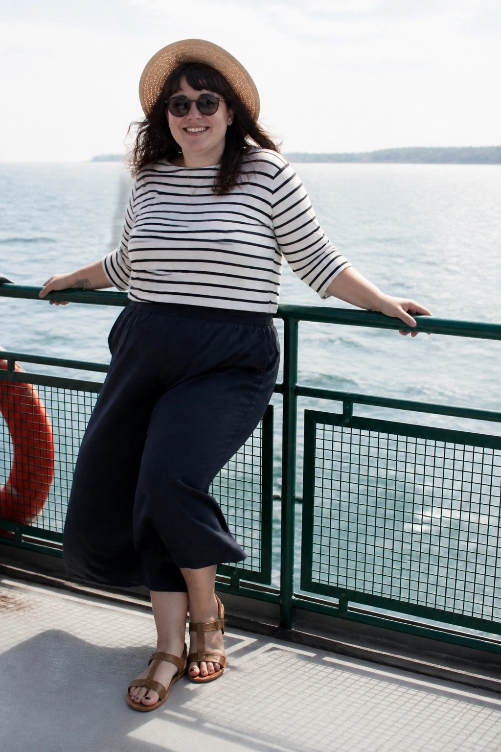 Woman in striped shirt and straw hat leaning on green railing by water