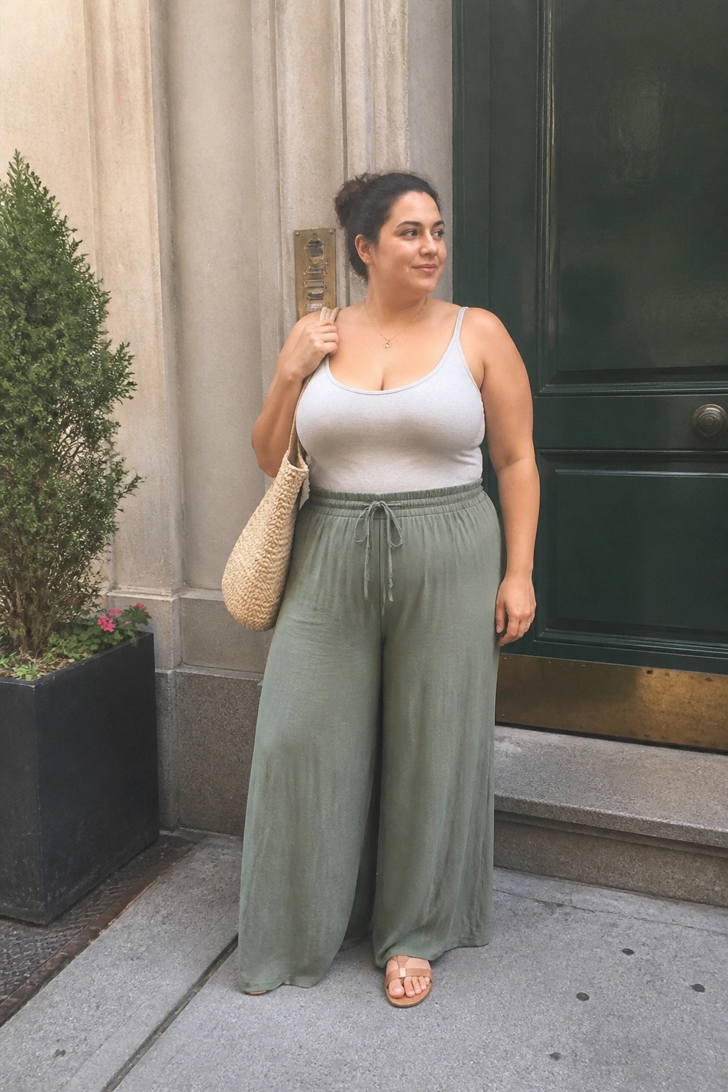 Woman in gray tank top and sage green wide-leg pants holding woven bag outdoors
