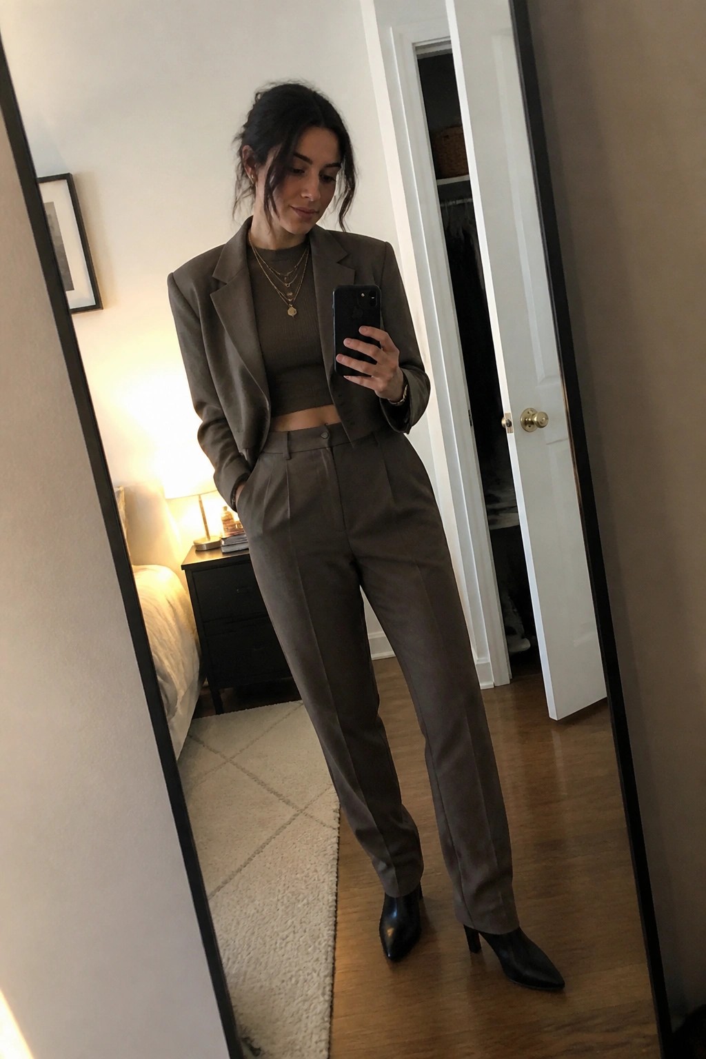 Woman in taupe cropped blazer and trousers takes mirror selfie in bedroom