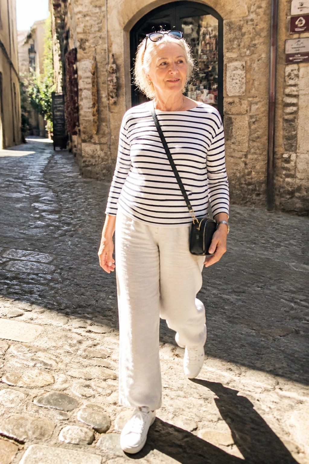 Elderly woman in striped shirt and white pants on cobblestone street