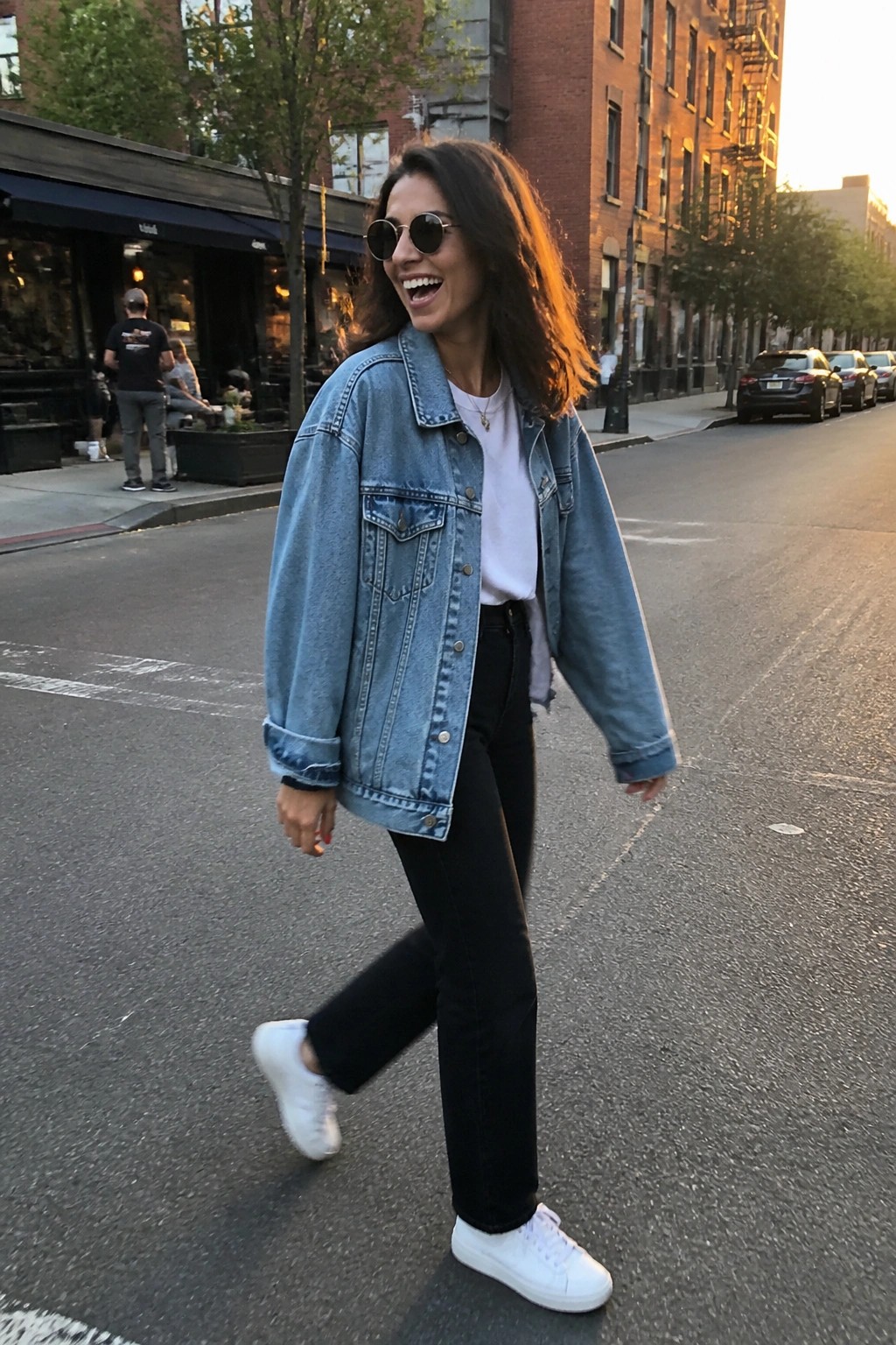 Smiling woman in light blue denim jacket and black jeans on city street