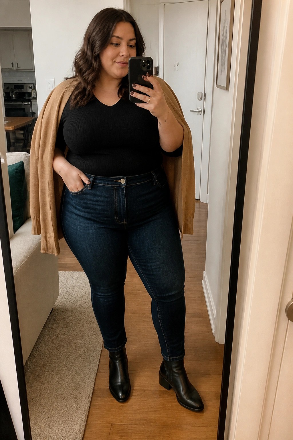 Woman in black top, blue jeans, tan cardigan taking mirror selfie with phone