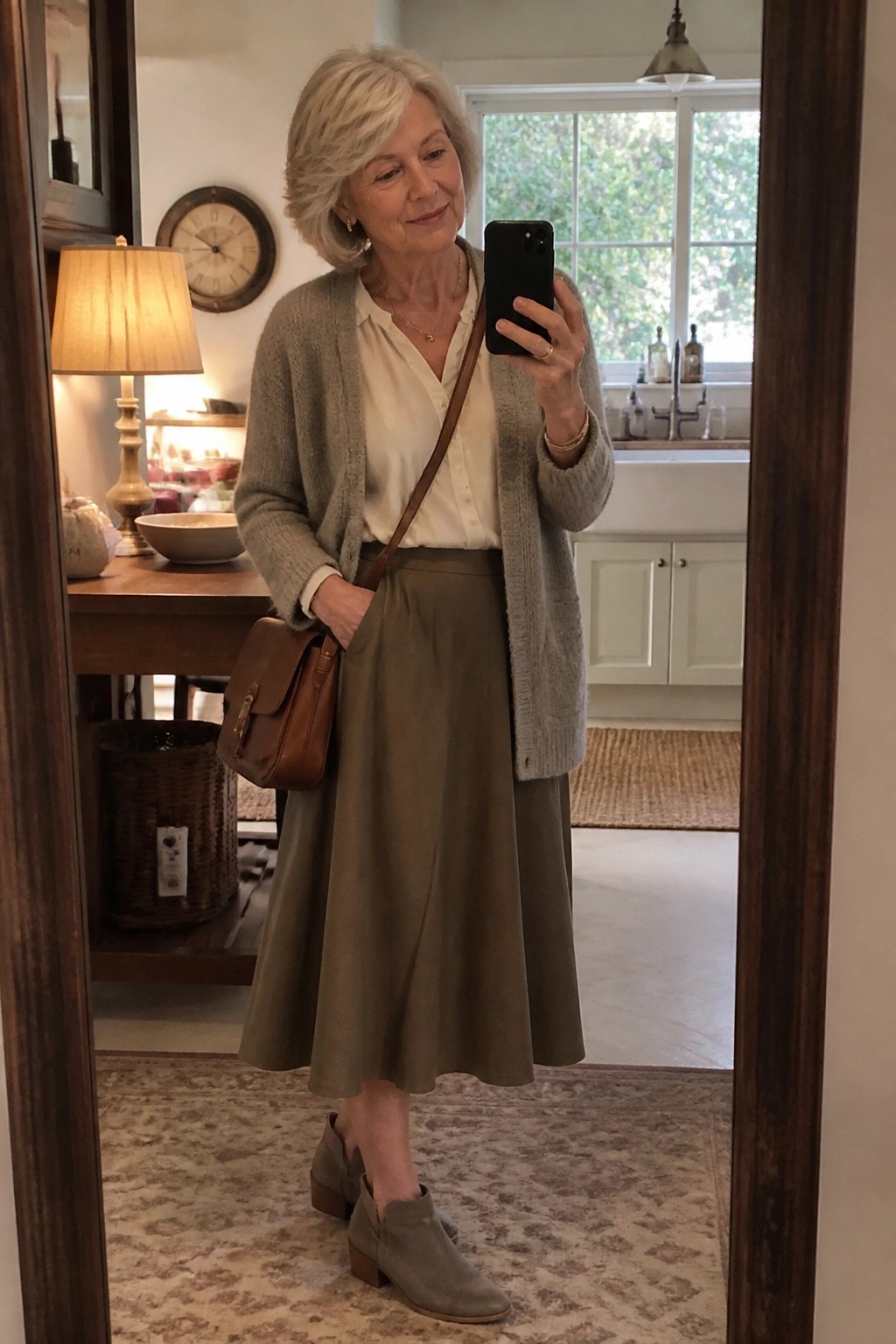 Elderly woman in gray cardigan and olive skirt taking mirror selfie in home
