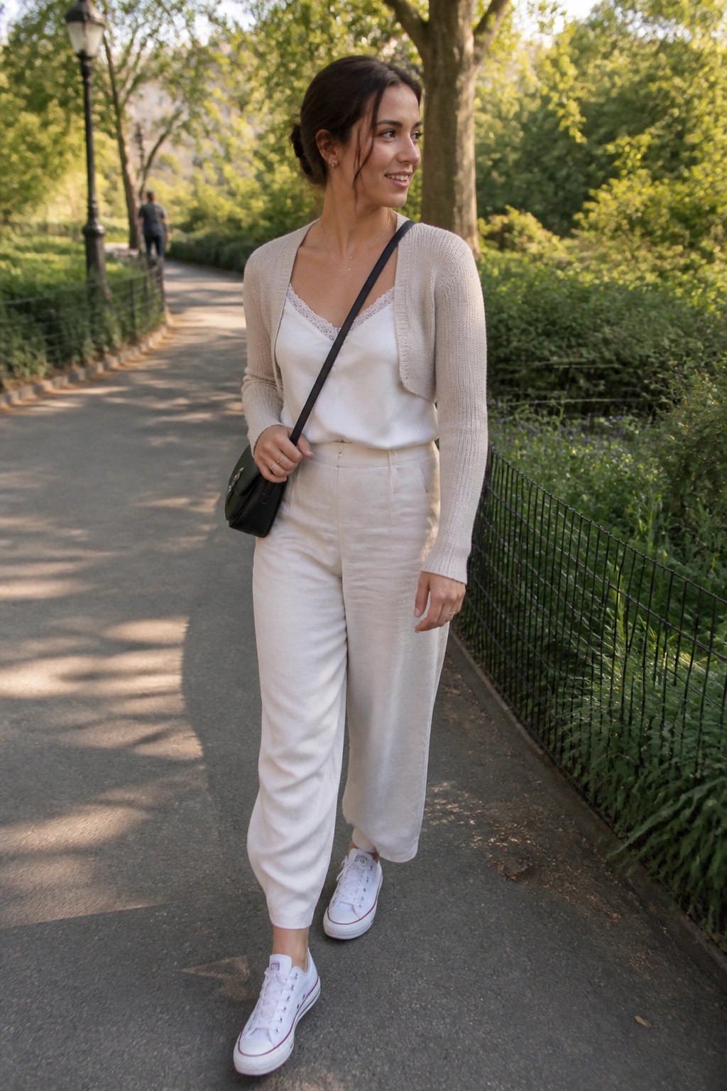 Woman in white outfit and beige cardigan walking on sunny park path