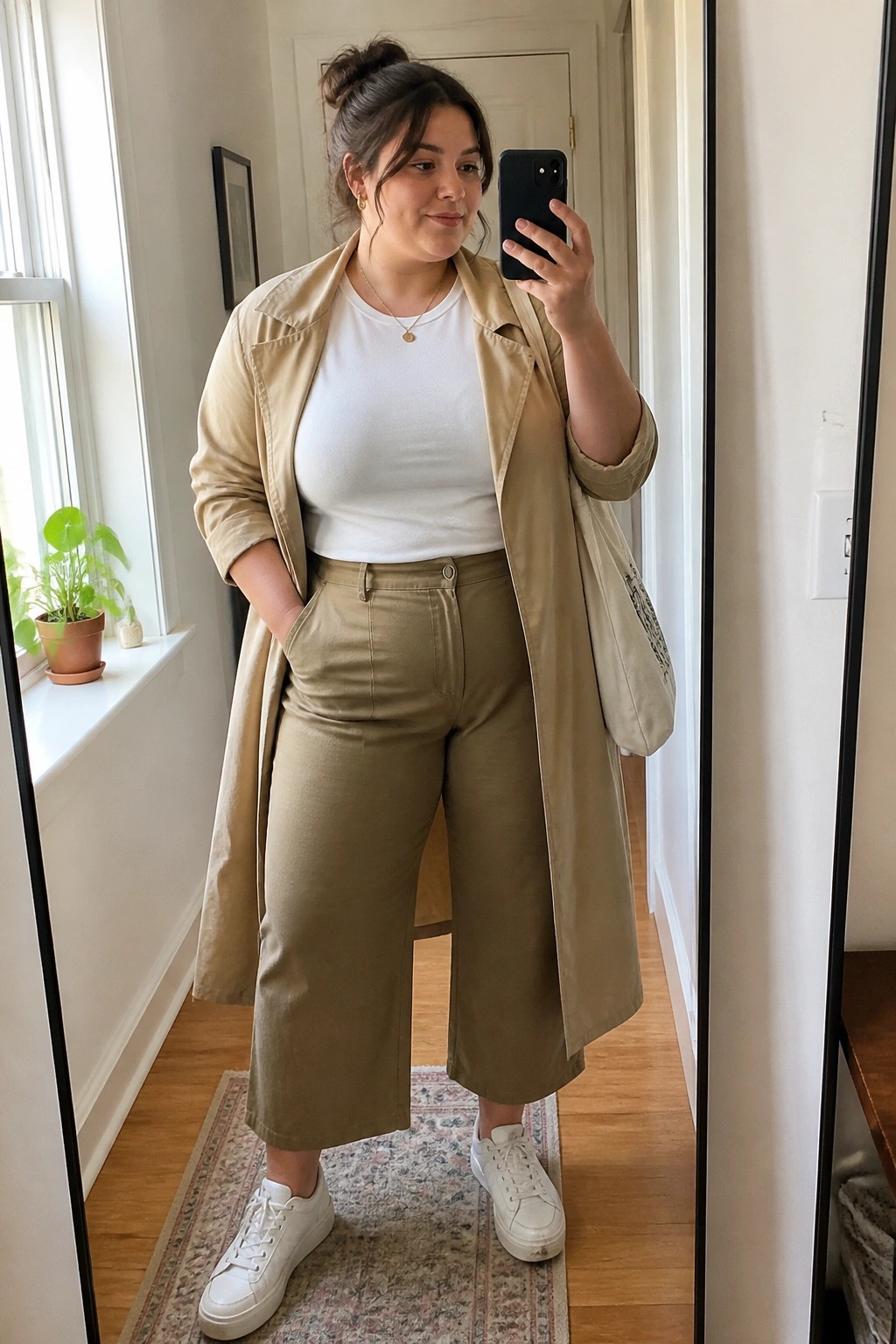 Woman in beige trench coat, white tee, olive pants taking mirror selfie.
