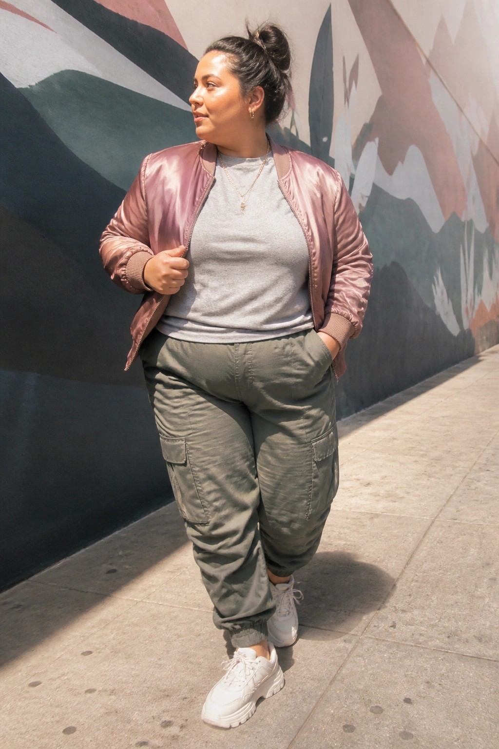 Woman in pink bomber jacket and green cargo pants by colorful mural wall