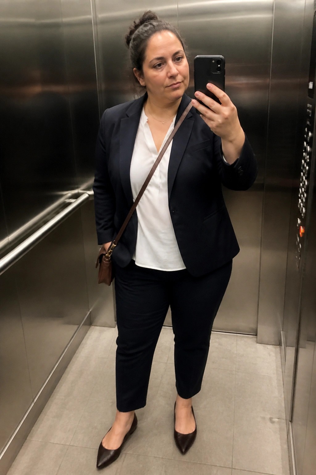 Woman in navy blazer taking selfie inside stainless steel elevator